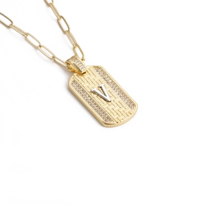 Gros plan détaillé d'un collier doré avec pendentif texturé, lettre V et petits diamants