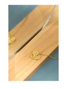 Detailed macro view of a heart-shaped angel pendant in gold finish on a wooden tray