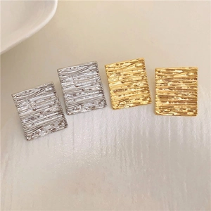 Macro detail of geometric square earrings with textured metallic ripple surface finish
