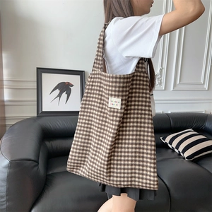 Detail showing the brown checkered texture and designer logo patch on the tote bag