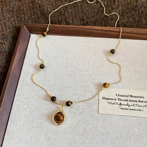 Vintage gold necklace with tiger eye flower pendant and beads on a beige display