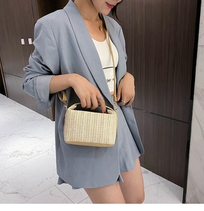 Model wearing a woven straw crossbody bag with brown leather trim in a minimalist setting
