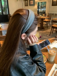 Side view of a grey-green fabric wide headband worn in a cozy cafe setting