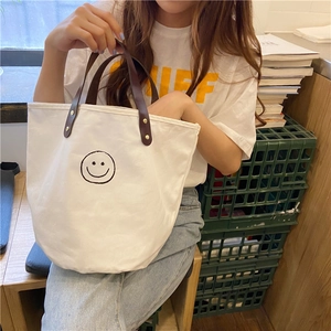 Close-up of vintage canvas bucket bag featuring a hand-drawn smiley and brown leather handle