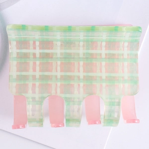 Detail of square hair claw with green and white plaid pattern and pink teeth