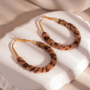 Detail of leopard print plush hoop earrings with golden metal clasps on white stone