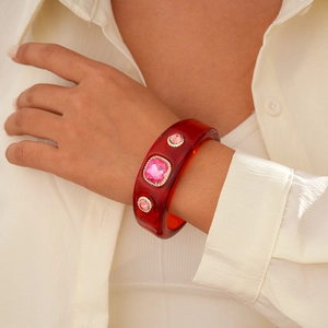 Macro shot of red resin wide cuff bracelet with pink gemstones and crystal accents