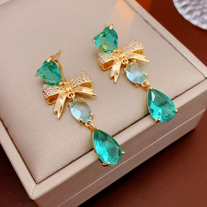 Close-up of golden bow earrings with green teardrop gemstones in a beige jewelry box