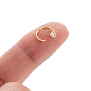 Detail of 0.8mm golden titanium C-shaped hoop with zircon, shown on finger for scale