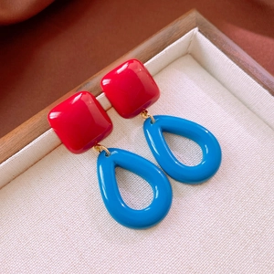 Detail view of geometric drop earrings featuring a red square stud and blue teardrop pendant