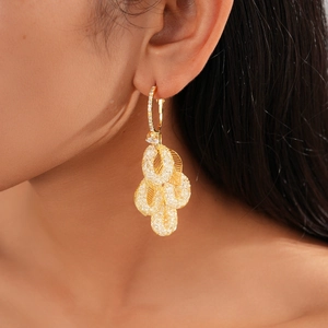 Close-up of golden tassel leaf earrings with zirconia stones worn by a female model