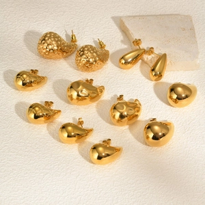 Minimalist gold teardrop earrings and organic metal studs on a textured stone base