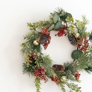 Christmas wreath with green pine needles, red berries, pine cones and gold bells on white