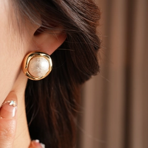Close-up of a model wearing a vintage gold plated round earring with a white pearl center