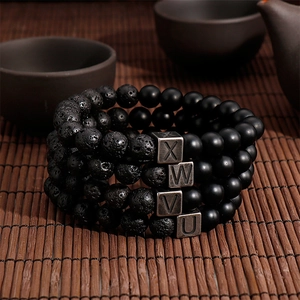 Detail of four-layered volcano stone bead bracelets with X W V U engraved metal charms
