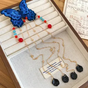 Pince à cheveux papillon brodée bleue avec pompons dorés dans une boîte à bijoux en bois