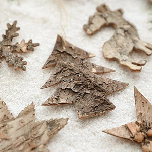 Natural wood bark Christmas ornaments in tree and reindeer shapes on white snow backdrop