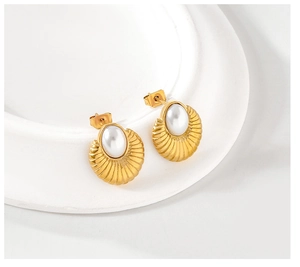 Detailed close-up of golden shell-textured earrings with oval pearl inlay on a white stand