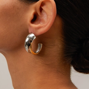 Close-up of chunky two-tone C-shape hoop earrings in polished gold and silver finish