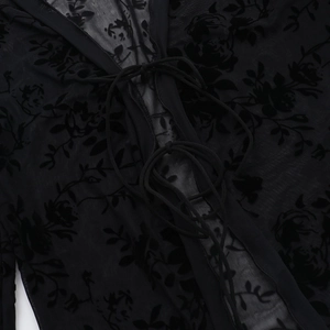 Detailed close-up of sheer black lace fabric with floral flocking and tie-neck design