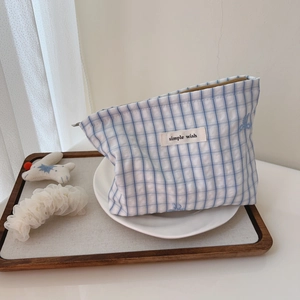 Close-up of blue plaid cotton bag with zipper and simple wish label on white plate