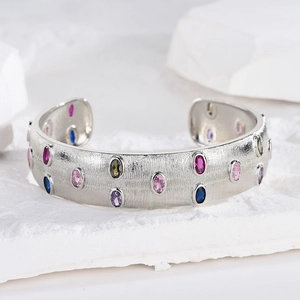 Detail of a brushed silver bangle set with colorful gemstones on a white stone background