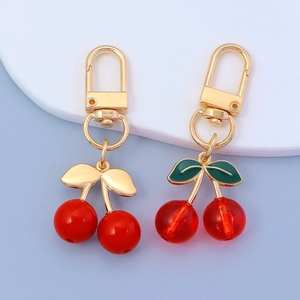 Cute cherry pendant keychains with red resin beads and golden metal leaves on blue background