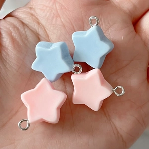 Close-up of four colorful resin star charms with metal rings held in a hand for DIY jewelry