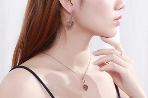 Macro view of silver tone MOM heart earrings and necklace set worn by a model