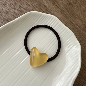 Detail of yellow resin heart charm on black elastic hair tie inside a white ceramic bowl