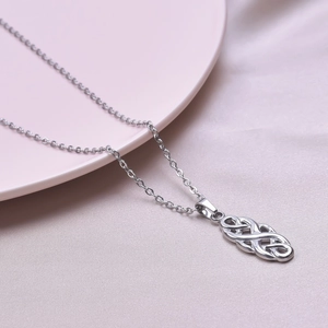 Detailed macro shot of a silver celtic knot pendant on a fine chain over a porcelain plate