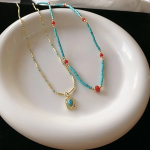 Detail of bohemian turquoise gold pendant and blue beaded necklace on ceramic tray