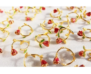 Close-up of handmade red enamel rose charms with golden leaves on white fabric