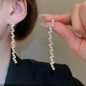 Detailed view of gold S-wave tassel earrings with zircons shown on model and held in hand