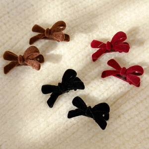 Flat lay of velvet bow hair clips in red, brown, and black colors on knit fabric