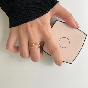 Detailed view of an irregular gold open ring with beads worn by a hand on a minimal background