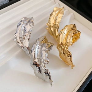 Close-up of gold and silver metallic leaf earrings with textured crumpled surface finish