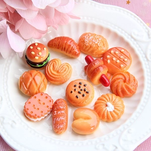 Close-up of miniature resin food charms including burgers and bread in a white tray