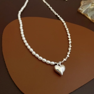 Détail du collier avec pendentif cœur argenté, perles et maillons sur fond de cuir