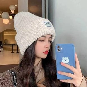 Detail view of cream-colored knit beanie with blue square patch decoration