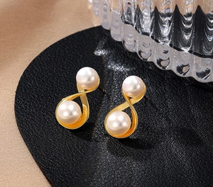 Macro view of gold infinity cross earrings featuring elegant white pearls on a surface