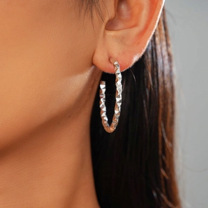 Close-up of silver geometric hoop earrings with textured facets on a model