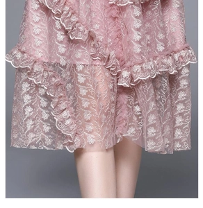 Détail d'une robe en dentelle rose brodée avec des volants superposés et fleurs