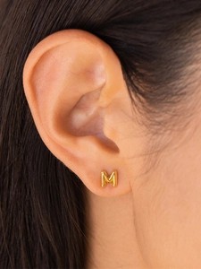 Detail shot of a minimalist gold-plated letter M stud earring worn by a model
