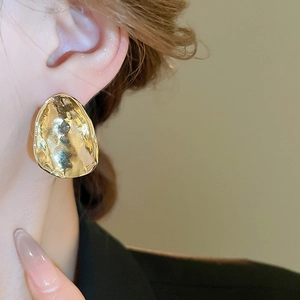 Close-up of a large irregular gold metal earring with lava texture worn by a model