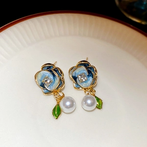 Detailed close-up of blue rose earrings with diamonds and pearls on a white plate