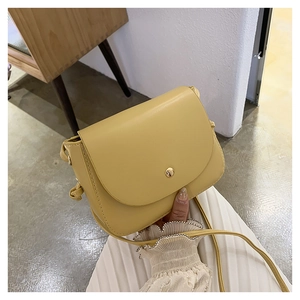Detail of yellow small square crossbody bag with gold button closure and leather texture