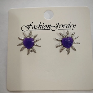 Detailed view of silver sunburst stud earrings with purple heart centers on a card