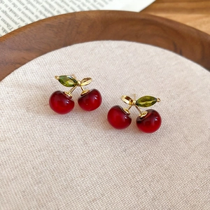 Detailed view of red cherry earrings with green leaves and gold stems on linen fabric