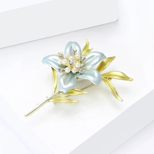 Close-up of lily brooch with blue enamel petals, pearls, and crystals on white backdrop